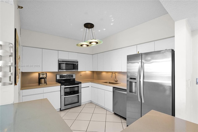 kitchen featuring appliances with stainless steel finishes, a sink, white cabinetry, decorative light fixtures, and light tile patterned floors