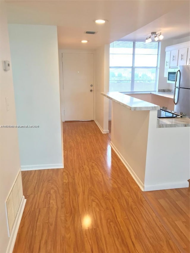kitchen with light countertops, freestanding refrigerator, light wood-type flooring, white microwave, and visible vents