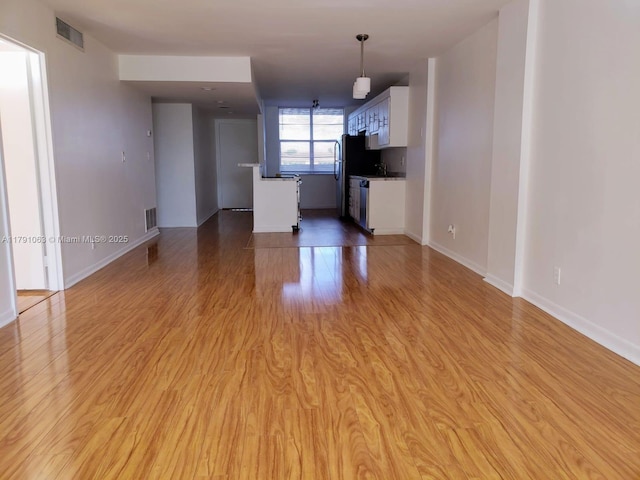 unfurnished living room featuring visible vents, baseboards, and light wood-type flooring