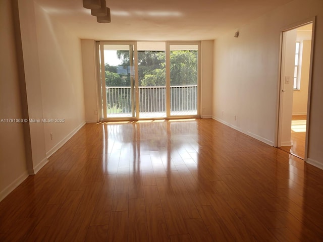 empty room featuring baseboards, dark wood-style flooring, and floor to ceiling windows