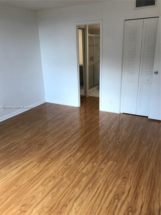 unfurnished bedroom with baseboards, a closet, wood finished floors, and visible vents