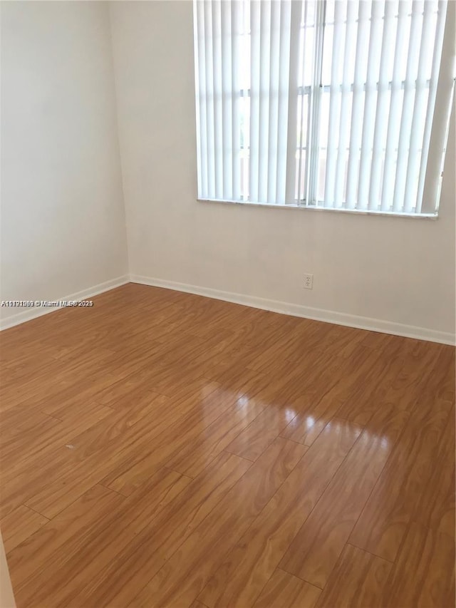 spare room with baseboards and wood finished floors