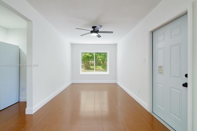 tiled empty room featuring baseboards and a ceiling fan