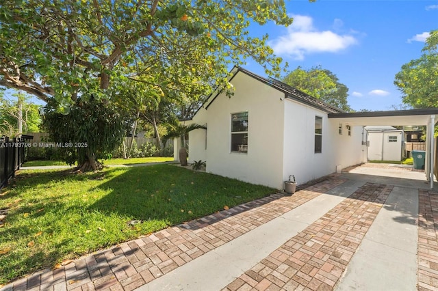 exterior space with driveway, a carport, fence, a yard, and stucco siding
