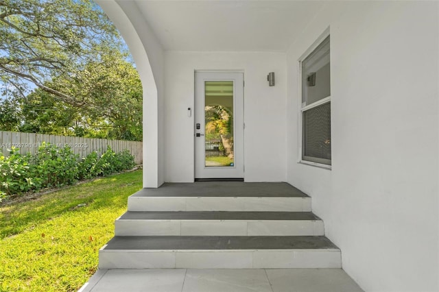 entrance to property featuring a lawn, fence, and stucco siding
