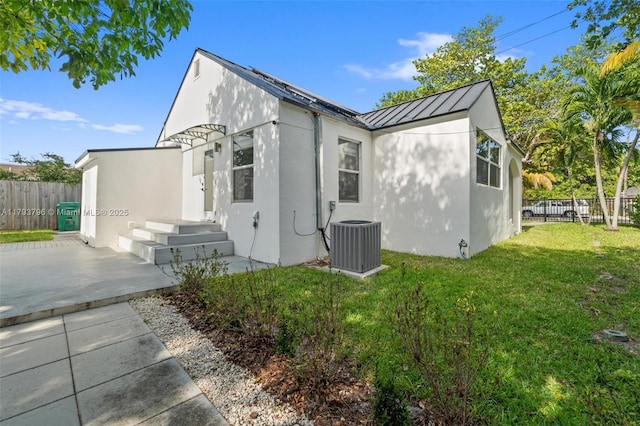 exterior space featuring fence, stucco siding, central AC unit, a standing seam roof, and a yard