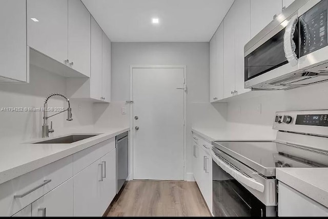 5401 Collins Ave Unit 411, Miami Beach, FL 33140 - kitchen featuring a sink, light countertops, light wood finished floors, stainless steel appliances, and white cabinetry