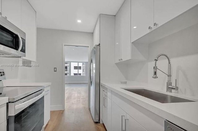 5401 Collins Ave Unit 411, Miami Beach, FL 33140 - kitchen with light wood-type flooring, light countertops, white cabinets, a sink, and stainless steel appliances