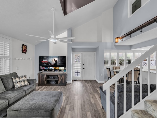 living room with stairs, wood finished floors, baseboards, ceiling fan, and high vaulted ceiling