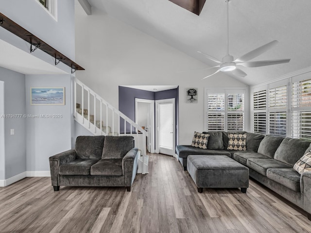 living area with high vaulted ceiling, a ceiling fan, stairs, and wood finished floors