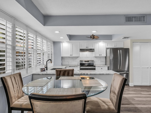 dining area featuring a raised ceiling, ceiling fan, wood finished floors, and visible vents