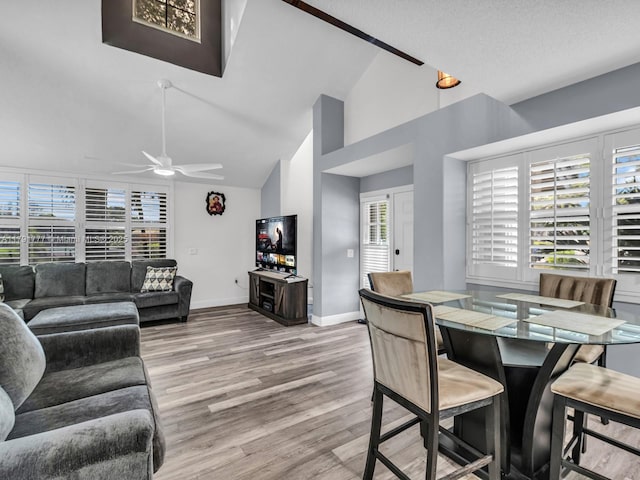 dining space with baseboards, a ceiling fan, light wood finished floors, and high vaulted ceiling