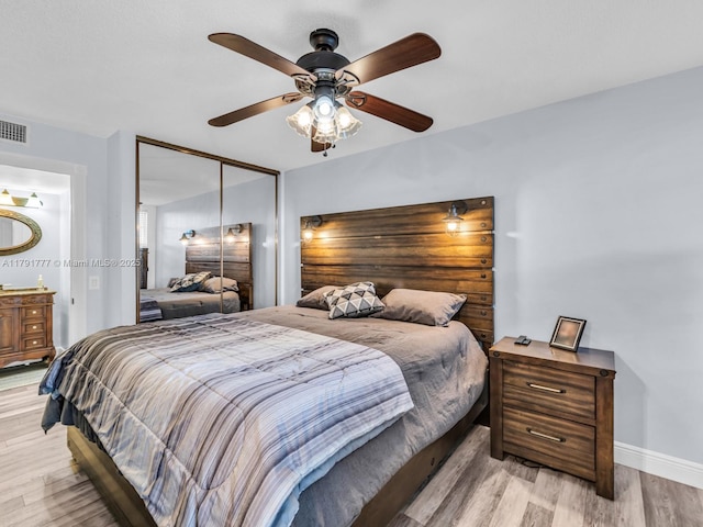 bedroom with ceiling fan, light wood-style floors, baseboards, visible vents, and a closet