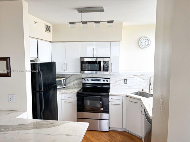 kitchen with appliances with stainless steel finishes, a sink, visible vents, and light stone counters