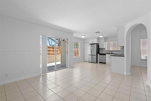 unfurnished living room with a healthy amount of sunlight, arched walkways, light tile patterned flooring, and visible vents