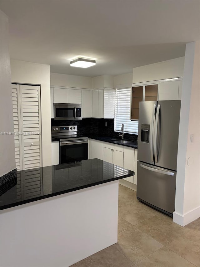 kitchen with dark countertops, baseboards, white cabinets, a sink, and appliances with stainless steel finishes