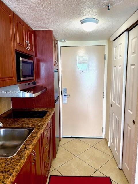 kitchen with a textured ceiling, built in microwave, a sink, light tile patterned floors, and under cabinet range hood
