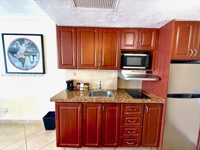 kitchen with decorative backsplash, a textured ceiling, a sink, freestanding refrigerator, and under cabinet range hood