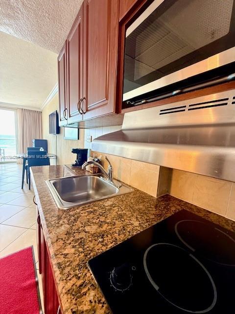kitchen with black electric cooktop, a textured ceiling, stainless steel microwave, a sink, and light tile patterned floors