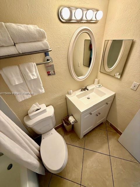 bathroom featuring tile patterned flooring, vanity, a textured wall, toilet, and baseboards