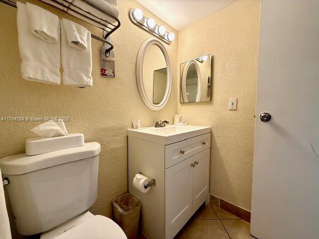 half bathroom with tile patterned floors, a textured wall, and toilet