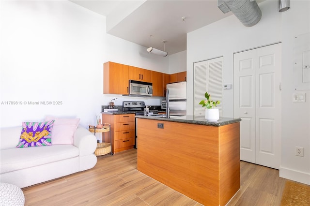 kitchen with appliances with stainless steel finishes, light wood-style flooring, an island with sink, brown cabinets, and a sink