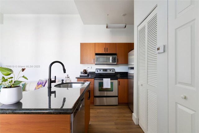 kitchen with stainless steel appliances, a sink, dark wood finished floors, and brown cabinets
