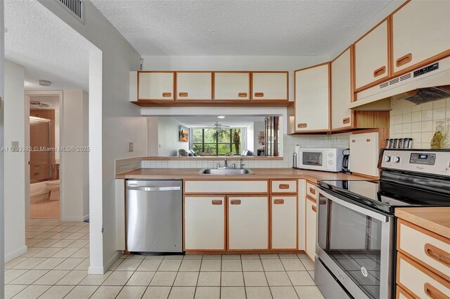 kitchen with a textured ceiling, visible vents, appliances with stainless steel finishes, a sink, and under cabinet range hood