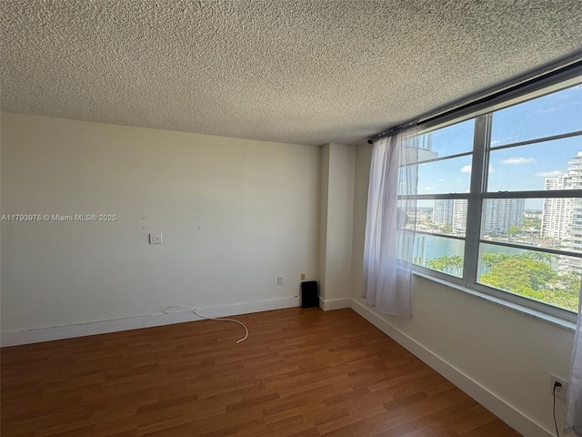 spare room featuring baseboards, a textured ceiling, plenty of natural light, and wood finished floors