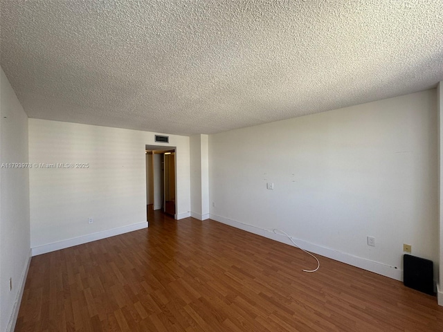 spare room with baseboards, visible vents, a textured ceiling, and dark wood-type flooring