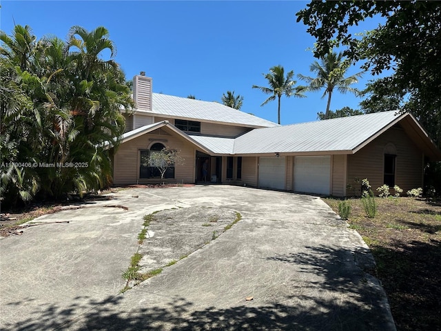 10737 SE Seaspray Ct, Hobe Sound, FL 33455 - view of front of home with a chimney, an attached garage, a metal roof, and concrete driveway