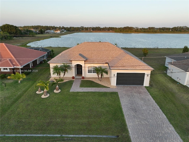 mediterranean / spanish house with a garage, a front lawn, decorative driveway, stucco siding, and a water view