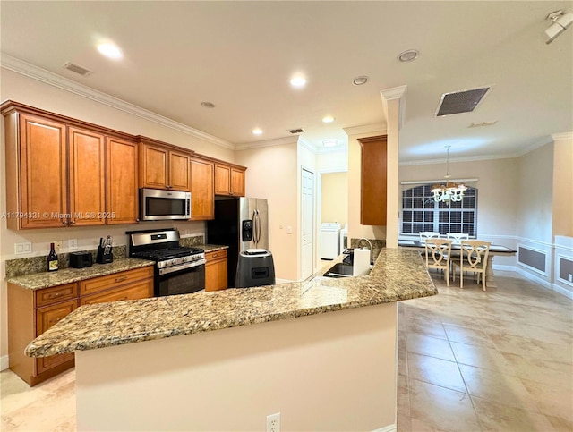kitchen featuring brown cabinetry, an inviting chandelier, washer and clothes dryer, a sink, and stainless steel appliances