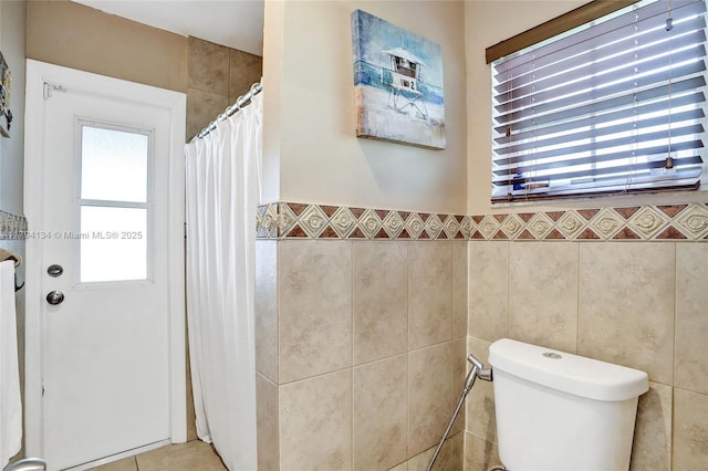 bathroom featuring a shower with shower curtain, toilet, and tile walls