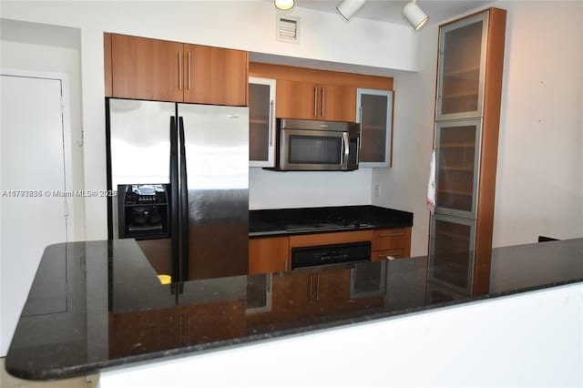 kitchen with visible vents, glass insert cabinets, brown cabinets, dark stone countertops, and stainless steel appliances