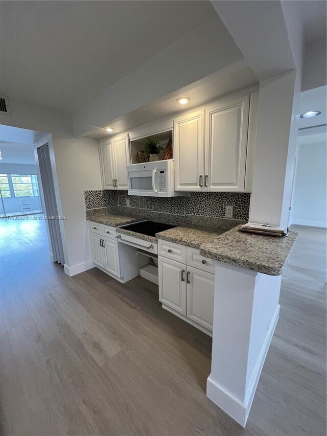 kitchen featuring open shelves, white microwave, baseboards, decorative backsplash, and light wood-type flooring