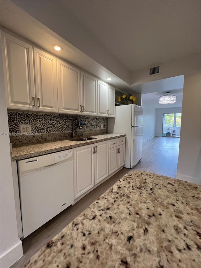kitchen featuring visible vents, white appliances, a sink, light wood finished floors, and backsplash