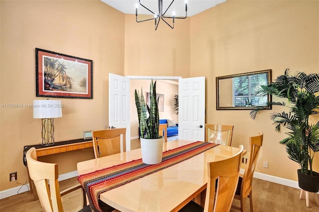 dining space featuring baseboards, a notable chandelier, wood finished floors, and a high ceiling
