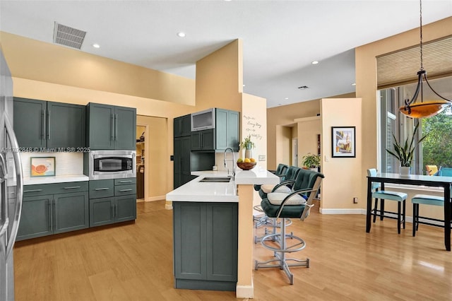 kitchen featuring visible vents, a sink, light countertops, stainless steel microwave, and light wood-style flooring