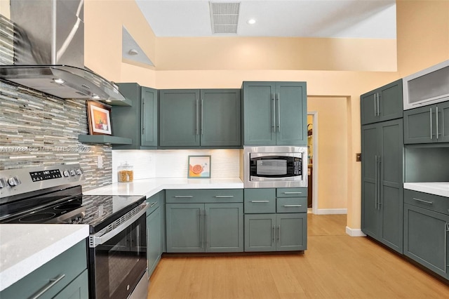 kitchen with visible vents, light wood-type flooring, light countertops, wall chimney exhaust hood, and appliances with stainless steel finishes