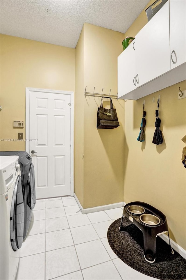 laundry area featuring a textured ceiling, cabinet space, light tile patterned floors, baseboards, and separate washer and dryer