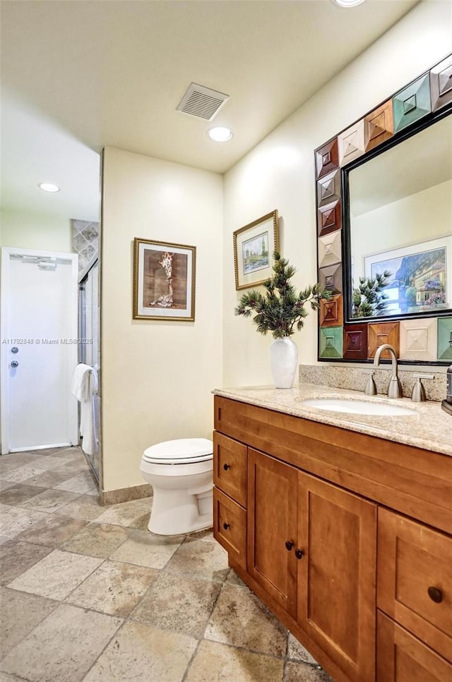 bathroom with vanity, toilet, stone tile flooring, visible vents, and a stall shower