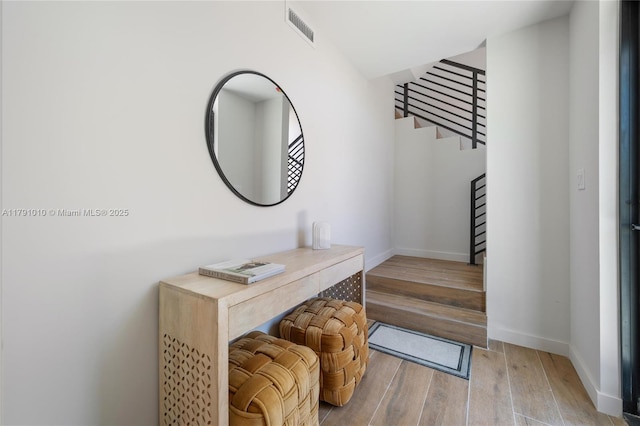 foyer entrance featuring visible vents, baseboards, wood finished floors, and stairway