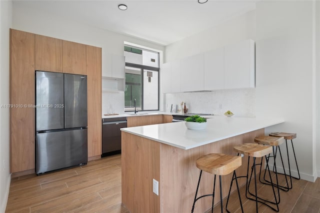kitchen with freestanding refrigerator, a peninsula, a breakfast bar, dishwashing machine, and modern cabinets