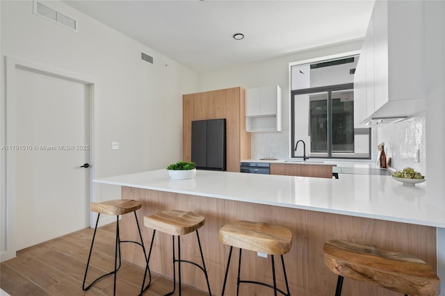 kitchen with a peninsula, light wood-type flooring, refrigerator, and visible vents