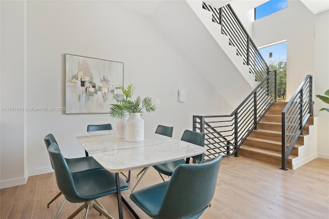 dining space with baseboards, a high ceiling, stairway, and light wood-type flooring
