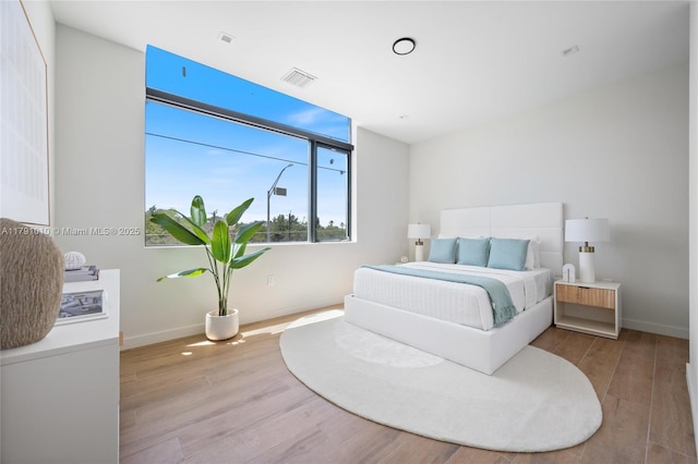 bedroom with baseboards, visible vents, and wood finished floors