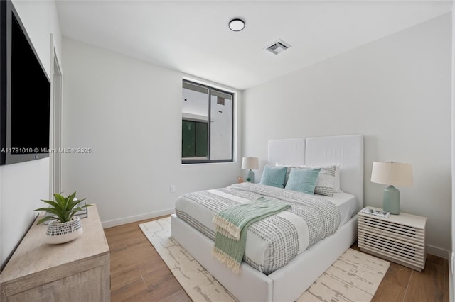 bedroom featuring baseboards, wood finished floors, and visible vents
