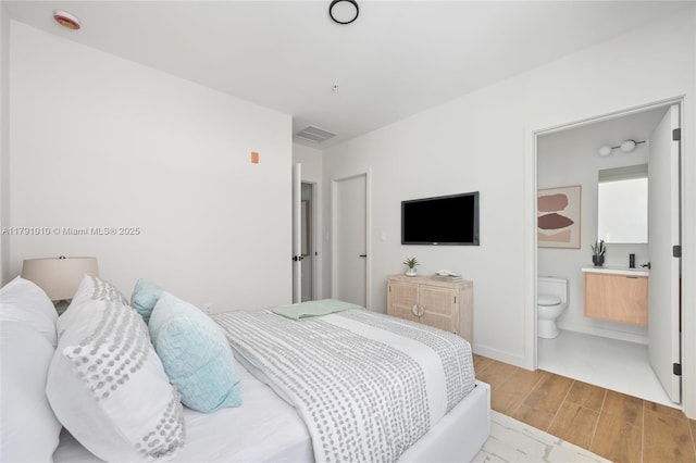 bedroom with visible vents, baseboards, ensuite bath, and wood finished floors