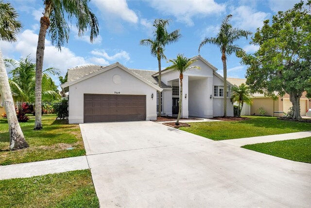 7649 Briar Cliff Cir, Lake Worth, FL 33467 - view of front facade with an attached garage, a front lawn, concrete driveway, and stucco siding